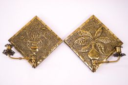 A pair of Arts and Crafts brass wall sconces each decorated with a vase of flowers and a brass