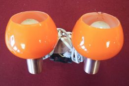 A 1970's orange glass light fitment with simulated copper frame holding two orange glass shades,