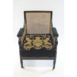 A Regency style black finished wood bergere armchair with curved back rail and padded arms