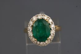 A yellow and white metal cluster ring set with an oval faceted cut emerald