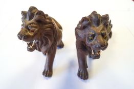 A pair of carved Asiatic hardwood stalking lions with inset glass eyes and bone teeth,