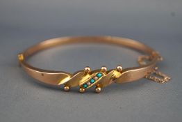 A yellow metal bangle set with turquoise and seed pearls having a push in clasp