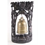 A brass temple bell, of traditional form, with naturalistic handle set on a carved hardwood stand,