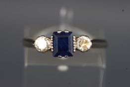 A white metal three stone ring set with a central rectangular cut sapphire