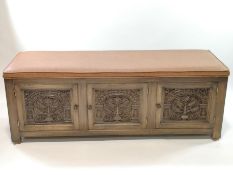An oak bench with upholstered leather seat above three carved cupboard doors 70cm high x 185cm wide