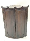 A 19th century oak hanging corner cabinet, the bow front opening to reveal two shelves,
