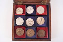 A wooden case containing nine assorted metal sporting prize medals fencing, long jump,