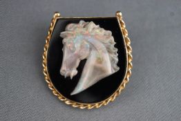 A yellow metal pendant/brooch in the design of a horseshoe set with black onyx and having a cameo