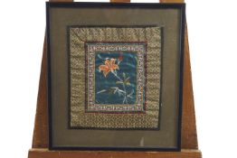 Two framed Chinese silk embroideries, each with a central flower spray on a blue ground,