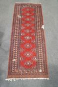 A Berber style runner with central shaped lozenge motifs on a claret ground rectangular panel
