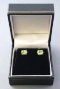 A white metal pair of single stone stud earrings. Each set with an oval faceted cut peridot.