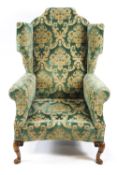 A scroll back wing armchair with shaped cresting and a curved seat front,