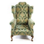 A scroll back wing armchair with shaped cresting and a curved seat front,