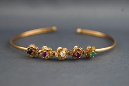 A yellow metal torque bangle having five interspaced flowers each set with a different gemstone