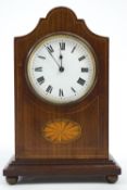 An Edwardian mahogany mantel clock with shaped dome top over a round white enamel Roman dial,