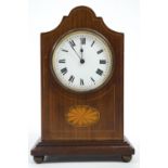 An Edwardian mahogany mantel clock with shaped dome top over a round white enamel Roman dial,