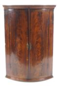 A George III mahogany bow fronted corner cabinet with flame mahogany and cross banding,