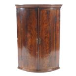 A George III mahogany bow fronted corner cabinet with flame mahogany and cross banding,