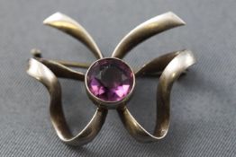 A white metal bow brooch set with amethyst