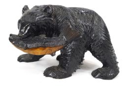 A carved Black Forest style bear with a fish in his mouth, ebonised and painted,