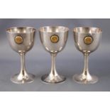 A trio of white metal egg cups, of plain form, raised on trumpet feet,