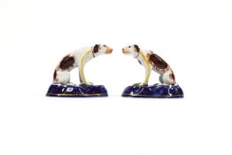 A pair of Staffordshire style figures of dogs each sitting on a shaped base