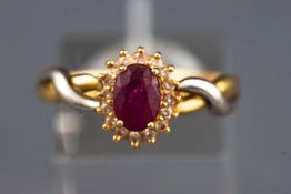 A yellow and white metal cluster ring set with an oval faceted cut ruby and surrounded by single