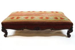 A large Victorian foot stool with carved cabriole legs, upholstered with tapestry bands and velvet,