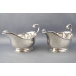 A pair of plain oval form silver sauce boats, with flying S scroll handles raised on plain rim feet,
