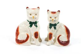 A pair of Staffordshire style cats, white with ginger patches and green neck bows,