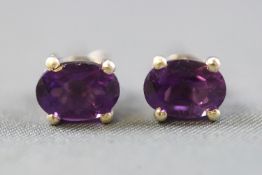 A white metal single stone pair of stud earrings, each set with an oval faceted cut amethyst.