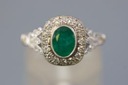 A white metal cluster ring set with an oval faceted cut emerald,