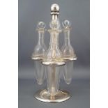 A silver three bottle cruet stand with ring slots for three collared plain glass vials,