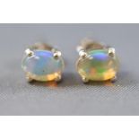 A white metal pair of single stone stud earrings, each set with an oval cabochon cut Ethiopian opal.