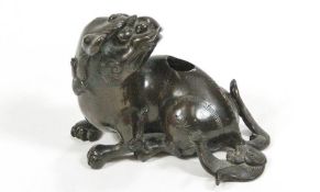 A bronze Dog of Fo figure, shown in a recumbent position, looking back over his shoulder,