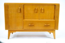 A G-Plan sideboard, in light oak, of plain rectangular form, set a tall cupboard,