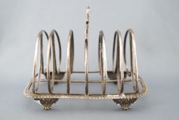 A silver toast rack with foliate strap handle over oval form separators on a gadrooned base