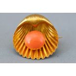 A yellow metal shell brooch set with a button shaped coral bead