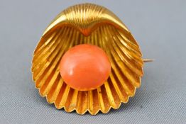 A yellow metal shell brooch set with a button shaped coral bead