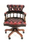 A red leather upholstered mahogany swivel Captains chair, on five wheeled legs,