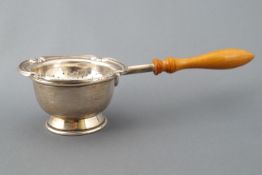 A silver tea strainer and stand, set with a wooden handle,