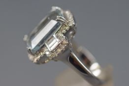 A white metal cluster ring set with a rectangular cut aquamarine