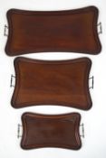 A set of three early 20th century mahogany shaped trays with brass handles,