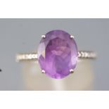 A white metal dress ring set with an oval faceted cut amethyst and finished with diamond shoulders.
