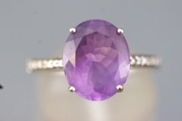 A white metal dress ring set with an oval faceted cut amethyst and finished with diamond shoulders.