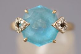 A yellow metal dress ring set with a chequerboard faceted cut blue topaz with diamond set accents.