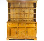 A pine dresser, the canted top with shaped cornice over three shelves, the base with two cupboards,