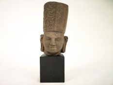 A Burmese carved stone bust, with traditional hat on a modern ebonised block base,