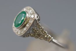 A white metal cluster ring set with an oval faceted cut emerald,