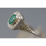 A white metal cluster ring set with an oval faceted cut emerald,